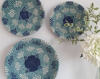 May include: Three woven wall baskets in various sizes with a blue and white pattern. The baskets are hanging on a white wall.