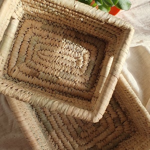 May include: Two woven rectangular baskets made of natural straw, one stacked on top of the other. The baskets have a light brown color and a natural, rustic look.
