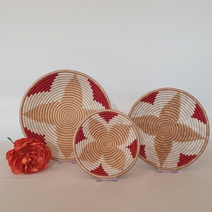 May include: Three woven baskets with a red and white geometric pattern. The baskets are nested inside each other, with the largest basket in the back and the smallest basket in the front.