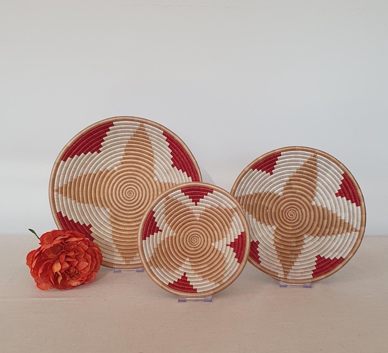May include: Three woven baskets with a red and white geometric pattern. The baskets are nested inside each other, with the largest basket in the back and the smallest basket in the front.