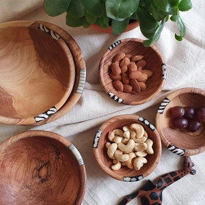 Puede incluir: Un juego de cuatro cuencos de madera con intrincados dise&ntilde;os en blanco y negro alrededor del borde. Los cuencos est&aacute;n llenos de almendras, anacardos, uvas y un utensilio de servir de madera con forma de jirafa.