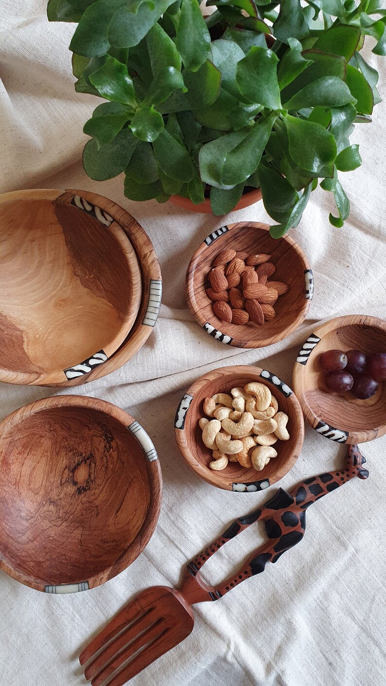 Puede incluir: Un juego de cuatro cuencos de madera con intrincados dise&ntilde;os en blanco y negro alrededor del borde. Los cuencos est&aacute;n llenos de almendras, anacardos, uvas y un utensilio de servir de madera con forma de jirafa.