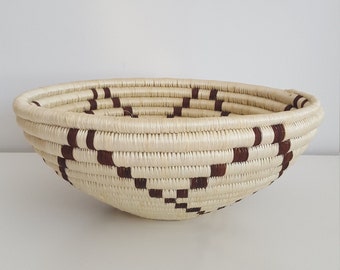 May include: A large, woven bowl with a brown and white geometric pattern. The bowl is made of natural materials and has a rounded shape.