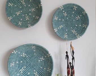 May include: Three teal blue woven wall baskets with white accents, a small potted plant, and a wooden figurine of three people.