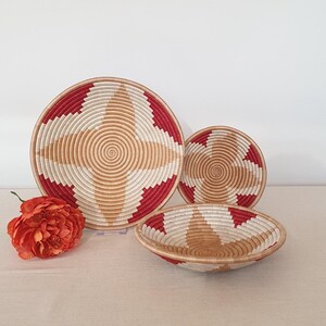 May include: Three woven baskets with a red and white geometric pattern. The largest basket is flat and the two smaller baskets are bowl-shaped.