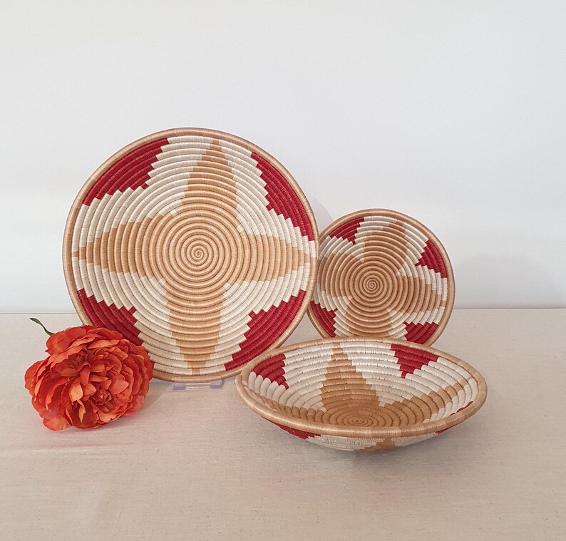 May include: Three woven baskets with a red and white geometric pattern. The largest basket is flat and the two smaller baskets are bowl-shaped.