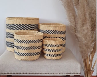 May include: Set of four woven baskets with blue and natural coloured stripes. The baskets are arranged in decreasing size on a light beige surface.