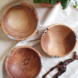 Puede incluir: Tres cuencos de madera con incrustaciones decorativas, uno con un patr&oacute;n de cebra, otro con un patr&oacute;n de rayas y otro con un patr&oacute;n marr&oacute;n y blanco. Tambi&eacute;n se muestra un utensilio de servir de madera con forma de jirafa.