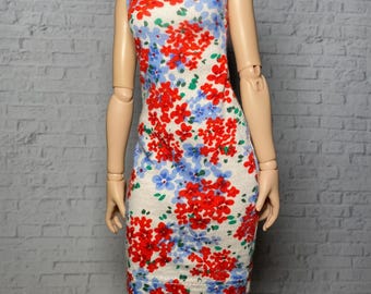 May include: A sleeveless, knee-length dress with a floral pattern. The dress features a white background with red and blue floral designs. The dress is form-fitting and has a scoop neckline.
