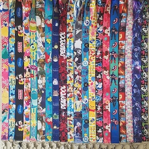 May include: A collection of colorful lanyards with various cartoon characters and designs, including Mickey Mouse, Monsters University, Totoro, Deadpool, and Winnie the Pooh. The lanyards are all approximately 1 cm wide and have a silver metal clip at the end.