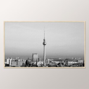 May include: A black and white photograph of the Berlin skyline, featuring the iconic Fernsehturm television tower in the centre. The photo captures a panoramic view of the city, including various buildings and structures.