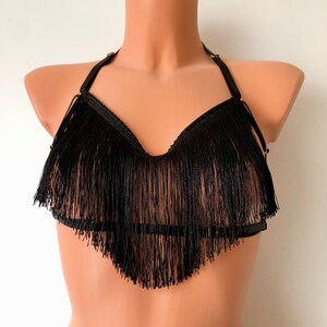 Puede incluir: Un sujetador negro con flecos y tirantes ajustables. El sujetador está hecho de un material suave y elástico y tiene un aspecto delicado y femenino.