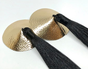 Copri capezzoli in similpelle color oro con nappe di seta nera spesse e lunghe.