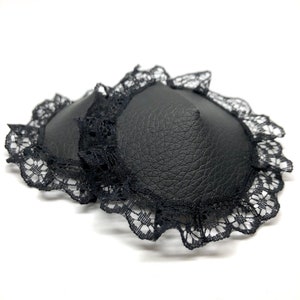 A pair of black faux leather nipple pasties with black lace rim