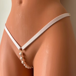 Puede incluir: Un conjunto de lencería blanco con un detalle de cadena de perlas. La lencería está hecha de una tela suave y elástica y tiene un diseño delicado y femenino.