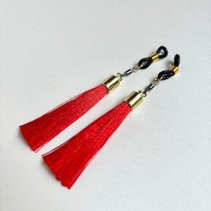 May include: Two red tassel eyeglass holders with gold-toned metal accents and black clasps.