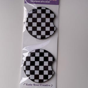 May include: Two car coasters with a black and white checkered pattern are displayed in a clear plastic package. The package has the text "CAR COASTERS handmade with LOVE!" and "Katie Rose Creative".