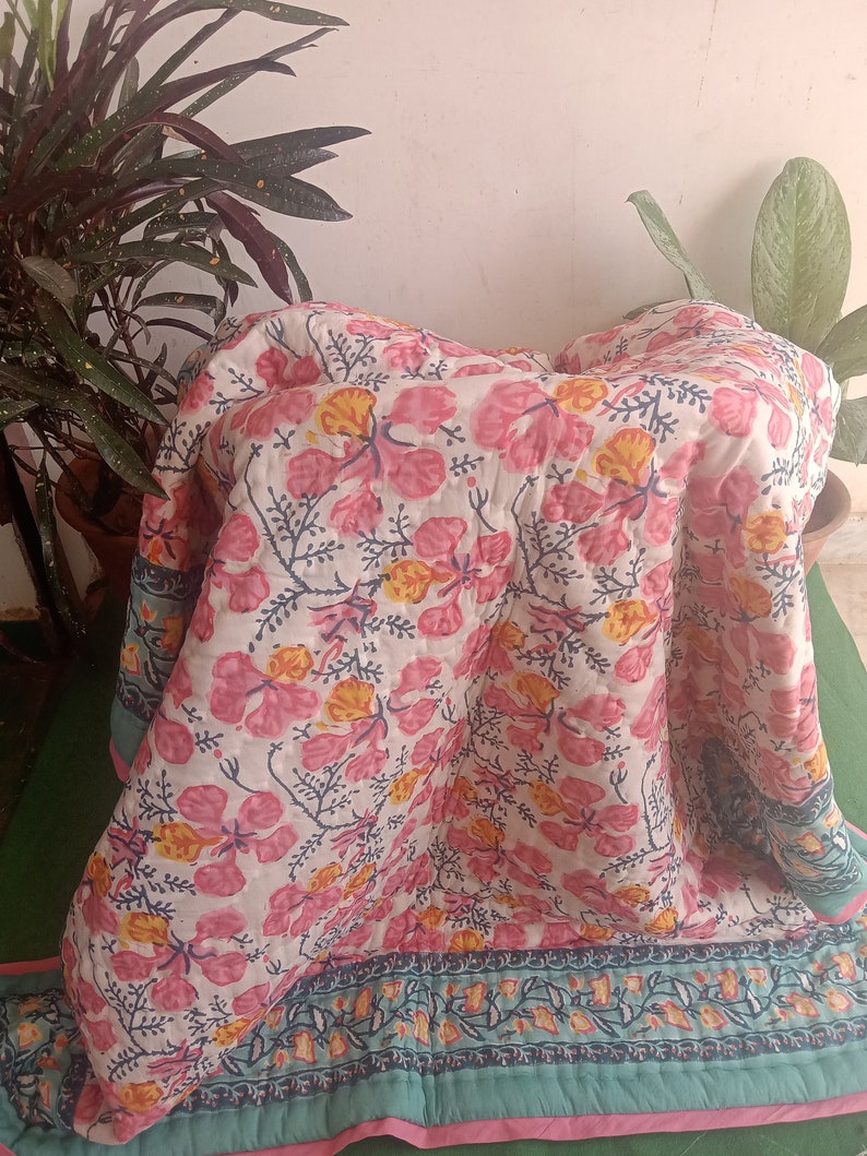 Pu&ograve; includere: Un piumino con motivo floreale rosa e bianco con un bordo verde acqua e bianco. Il piumino &egrave; piegato e appoggiato su una superficie verde.