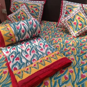 May include: A yellow, green, and red floral patterned quilt with a matching pillow. The quilt is folded and placed on a bed with other pillows.