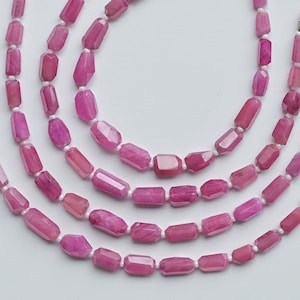 May include: Strands of pink gemstone beads with a rectangular shape, strung together. Each strand is accented with a bright pink tassel at the end. The beads are a vibrant shade of pink, and the tassels add a touch of flair.