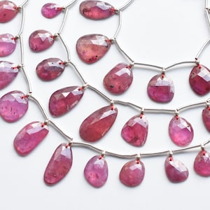 May include: A strand of pink gemstone beads with silver connectors and red tassels. The beads are faceted and have a teardrop shape.