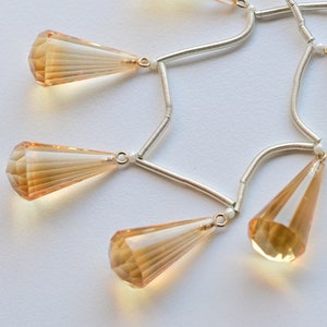 May include: A silver chain necklace with five teardrop-shaped, faceted, amber-colored crystals hanging from it.