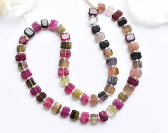 Könnte beinhalten: Eine Kette aus mehrfarbigen, quadratischen Turmalinperlen. Die Perlen sind eine Mischung aus Rosa, Grün, Schwarz und Braun.