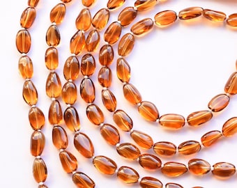 May include: A strand of oval-shaped, translucent, amber-colored gemstone beads. The beads are strung on a white cord and have a natural, polished finish.