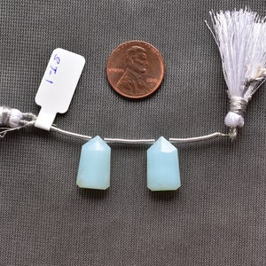 May include: Two light blue, faceted, teardrop-shaped gemstone beads strung on a silver wire with white tassels on either end. The beads are approximately the size of a UK penny.