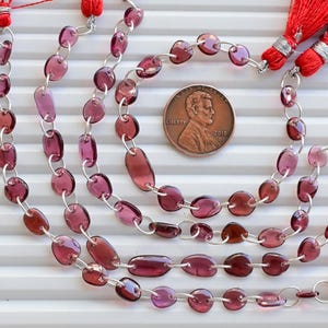 Könnte beinhalten: Eine Strähne aus violetten Edelsteinperlen mit silbernen Verbindungselementen. Die Perlen sind oval geformt und haben eine glänzende Oberfläche. Die Strähne ist lang genug, um sich mehrmals um ein Handgelenk oder einen Hals zu wickeln.