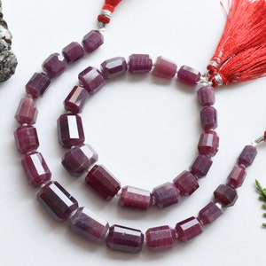 May include: Two strands of purple gemstone beads with faceted rectangular shapes. The beads are strung on a silver cord with red tassels at the ends.