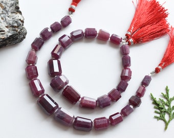 May include: Two strands of purple gemstone beads with faceted rectangular shapes. The beads are strung on a silver cord with red tassels at the ends.