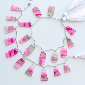 May include: Strands of pink and gray agate gemstone beads with a polished finish. The beads are strung on silver-colored wire and accented with white tassel pendants. The gemstones have a banded pattern.