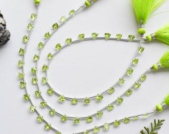 May include: Three strands of green peridot gemstone beads strung on silver wire. The beads are triangular in shape and are arranged in a repeating pattern. The strands are tied together at the ends with green tassels.