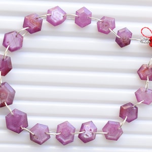 Può includere: Una collana di perline esagonali sfaccettate nei toni del rosa e del viola, infilate su filo d'argento. Le perline sono traslucide e la collana è rifinita con nappe rosse.