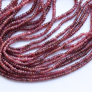 Pu&ograve; includere: Un filo di perle di rubino rosso scuro, ogni perla &egrave; sfaccettata e ha una forma leggermente arrotondata. Le perle sono infilate su un filo trasparente e sono disposte in un motivo sciolto e fluido.
