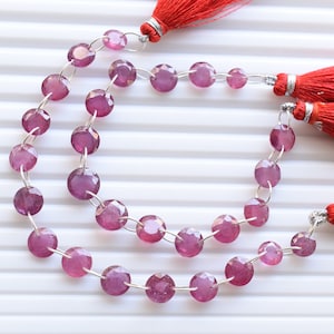 May include: A strand of pink gemstone beads with silver jump rings. The beads are round and faceted. The strand is finished with red tassels.