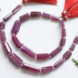 May include: A strand of faceted purple gemstone beads with silver clasps and red tassels. The beads are rectangular in shape and have a polished finish.
