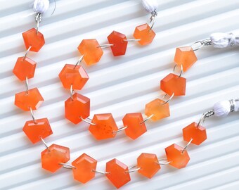 May include: A strand of orange carnelian gemstone beads, each bead is faceted and shaped like a hexagon. The beads are strung on silver wire and have white tassels on each end.