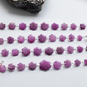 May include: Four strands of purple gemstone beads strung on silver wire with red tassels at the ends.