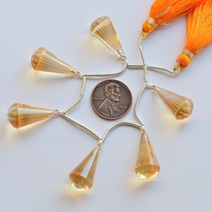 May include: A set of six teardrop-shaped faceted gemstone beads with silver-toned connectors and two orange tassels. The beads are arranged in a circle around a US penny.