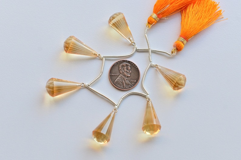 May include: A set of six teardrop-shaped faceted gemstone beads with silver-toned connectors and two orange tassels. The beads are arranged in a circle around a US penny.