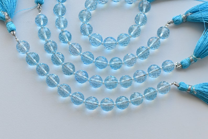 Puede incluir: Una hebra de cuentas de piedras preciosas de color azul claro con superficies facetadas. Las cuentas est&aacute;n enhebradas en un alambre de plata y tienen borlas en cada extremo.