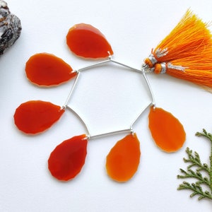 K&ouml;nnte beinhalten: Eine silberne Kette mit sechs orangefarbenen Karneol-Edelsteintropfen und einem doppelten orangefarbenen Quasten. Die Kette hat die Form eines Sechsecks.