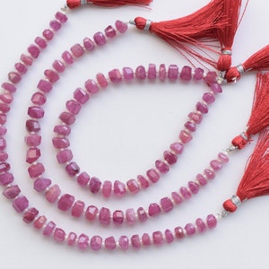 May include: Three strands of pink gemstone beads with silver clasps and red tassels. The beads are faceted and have a square shape.