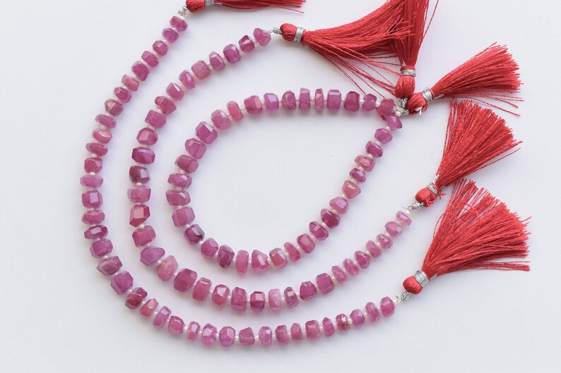 May include: Three strands of pink gemstone beads with silver clasps and red tassels. The beads are faceted and have a square shape.