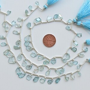 May include: Strands of light blue gemstone beads with silver accents and matching blue tassels. A penny is included for size reference. The beads are irregularly shaped and strung on silver wire.