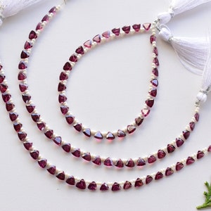 May include: Three strands of a necklace made with small, triangular, dark pink gemstones and white pearls. The necklace has white tassels on each end.