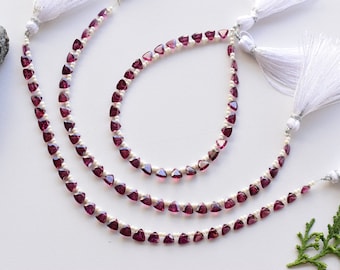 May include: Three strands of a necklace made with small, triangular, dark pink gemstones and white pearls. The necklace has white tassels on each end.