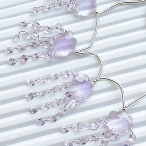 May include: A pair of silver earrings featuring amethyst stones. Each earring has a large amethyst stone in the centre, surrounded by smaller amethyst stones dangling from the bottom.